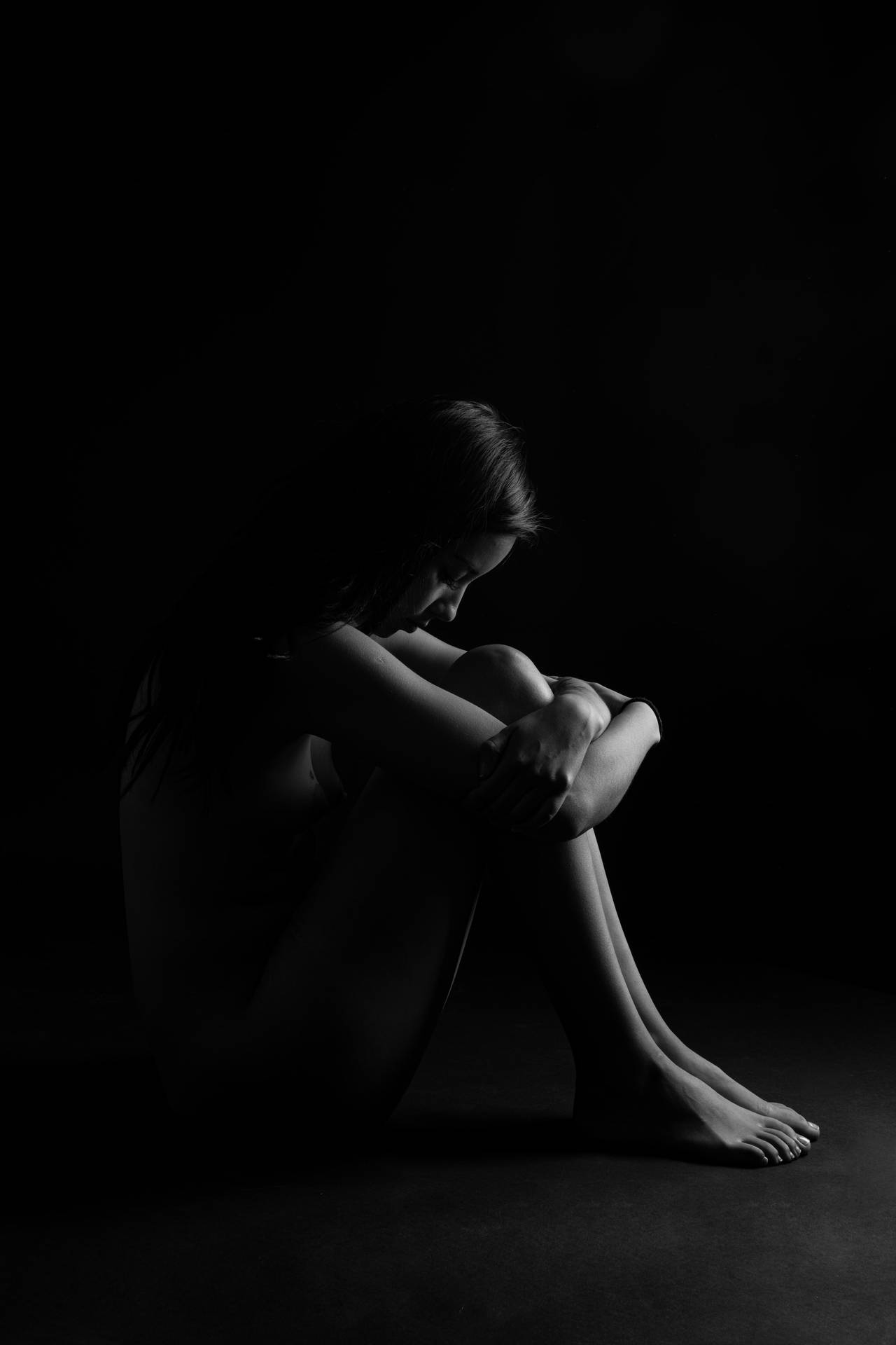 Black And White Portrait Of A Woman Sitting In The Dark Background