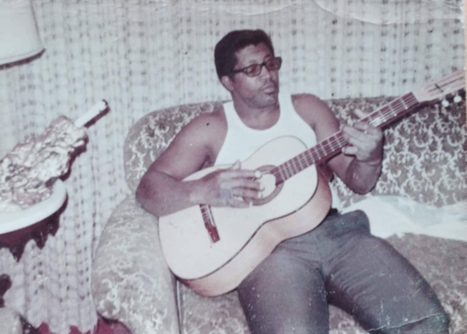 Bob Diddley Playing Guitar On Couch Background