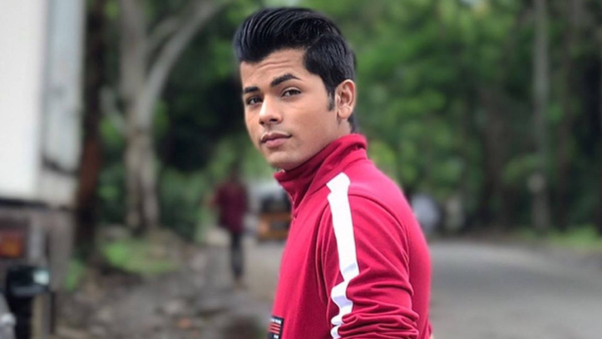 Bollywood Sensation Siddharth Nigam Striking A Pose In A Red Track Jacket Background