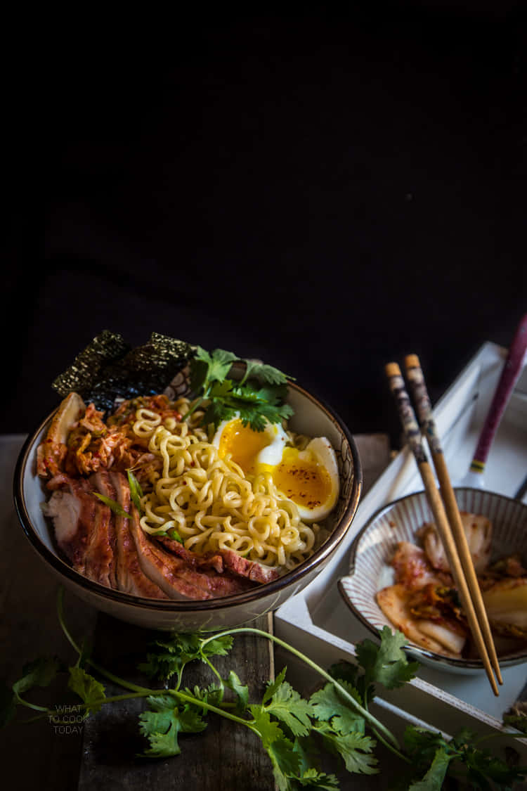 Bowl Of Ramen Beside Parsley And Kimchi Background