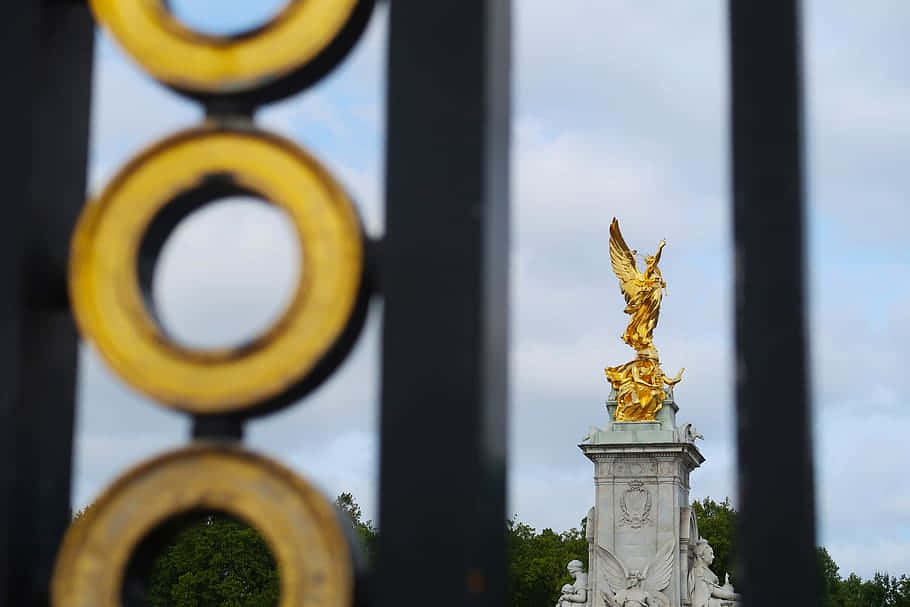 Buckingham Palace's Golden Statue Is Seen Through A Fence Background