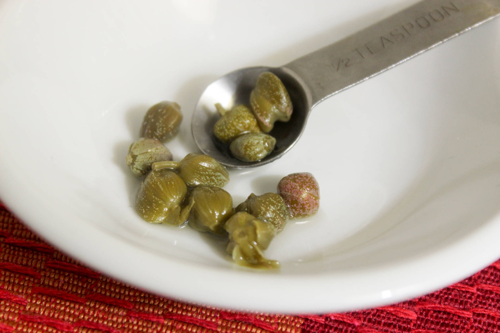 Capers In A Teaspoon On A White Bowl Background