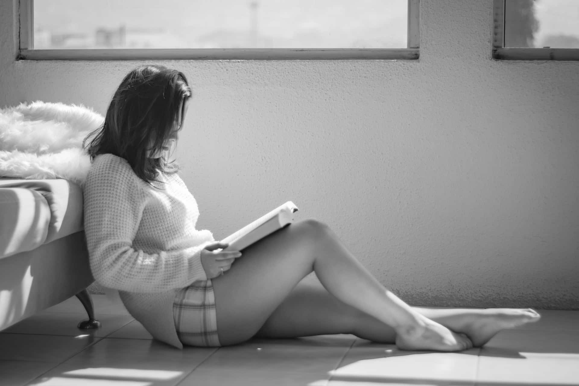 Caption: A Relaxed Woman Engrossed In Reading On A Leisure Day Background