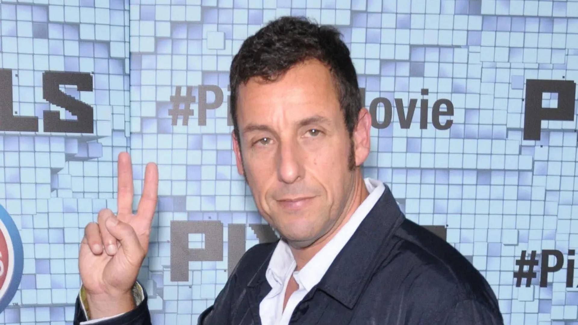 Caption: Adam Sandler Flashing A Peace Sign With A Charming Smile. Background