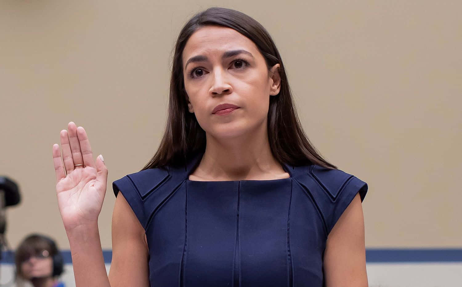Caption: Alexandria Ocasio-cortez Raising Her Hand In Passionate Speech Background