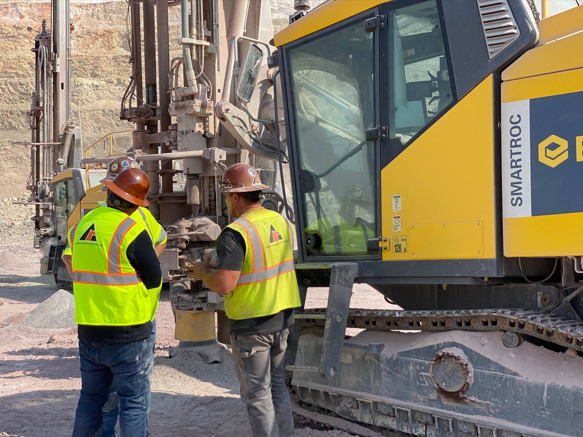 Caption: An Operator Manning A Blast-hole Drill On A Construction Site. Background