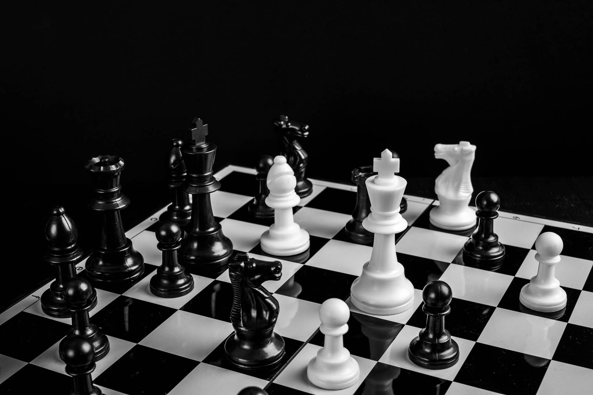 Caption: Engaging Mind Games: Black And White Plastic Chess Pieces On The Board Background