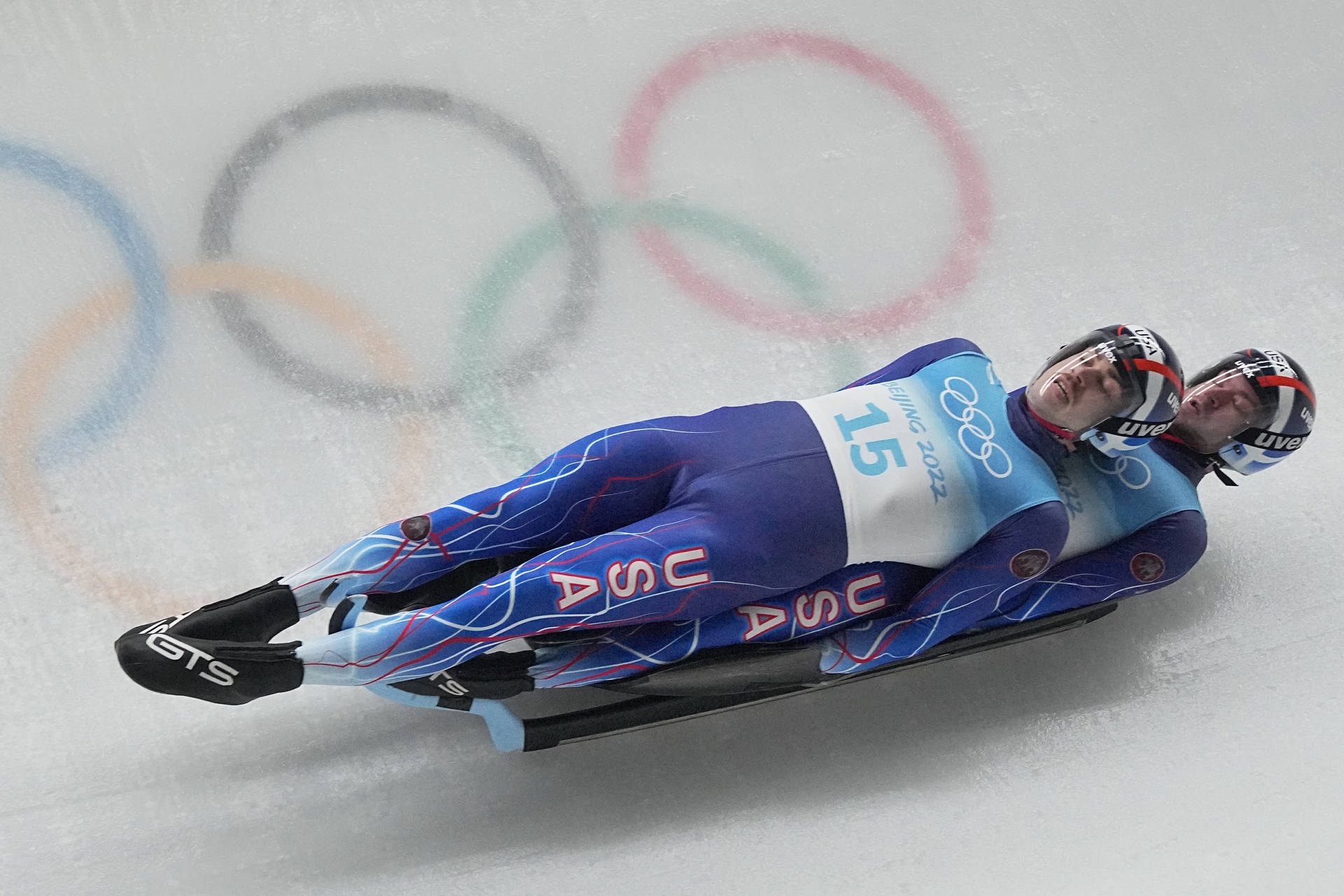 Caption: Intense Luge Doubles Action - Zachary Di Gregorio And Sean Hollander Background