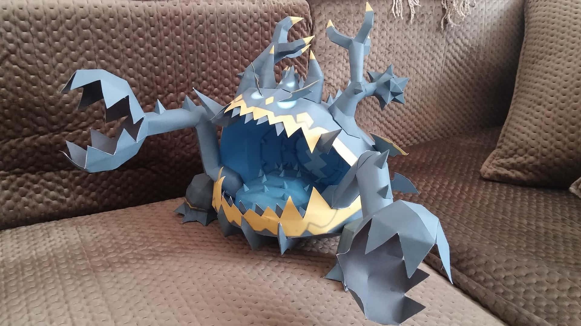 Caption: Intriguing Guzzlord Pokemon Figure On A Sofa Background