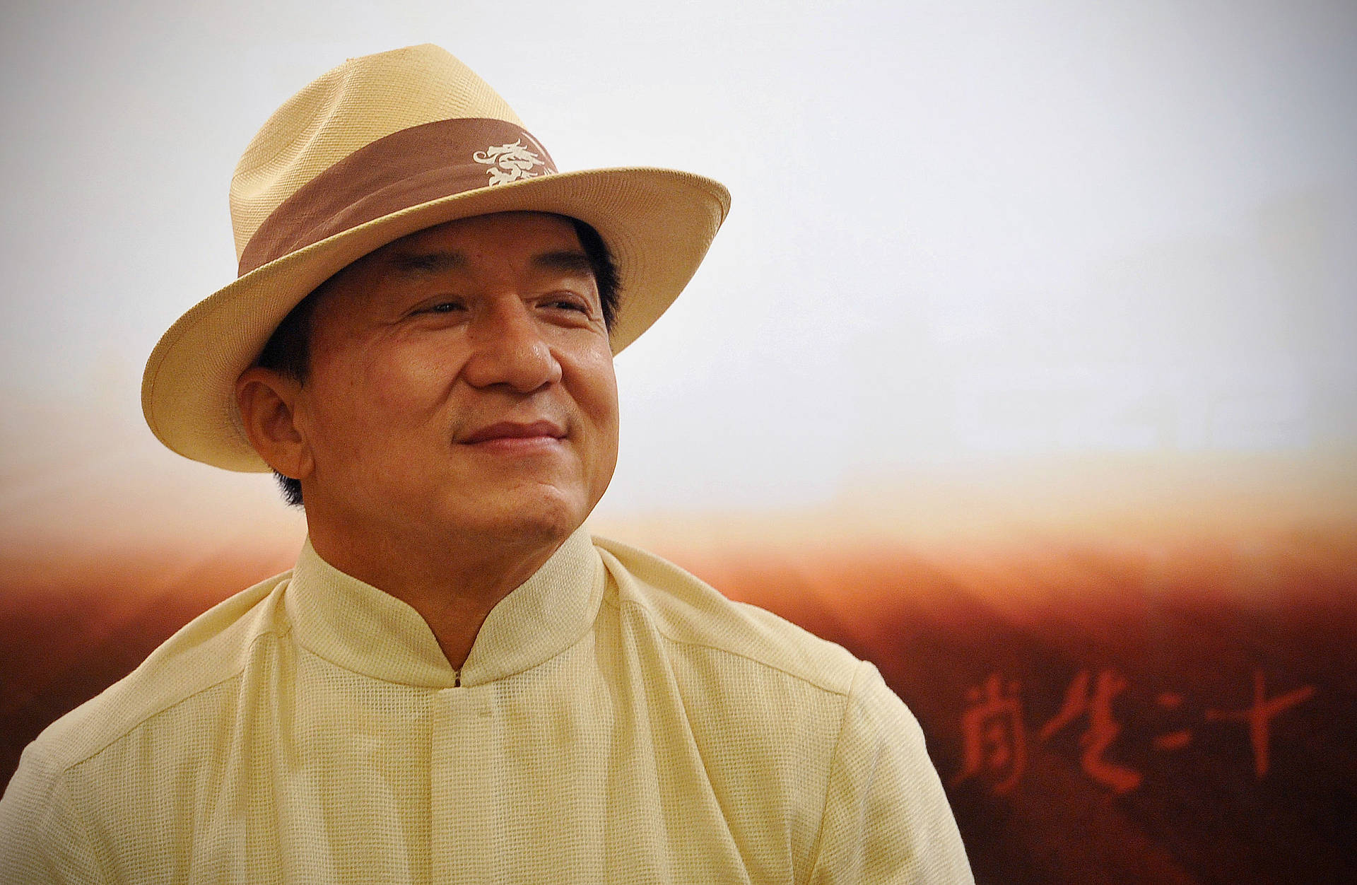 Caption: Legendary Jackie Chan In Traditional Woven Hat Background