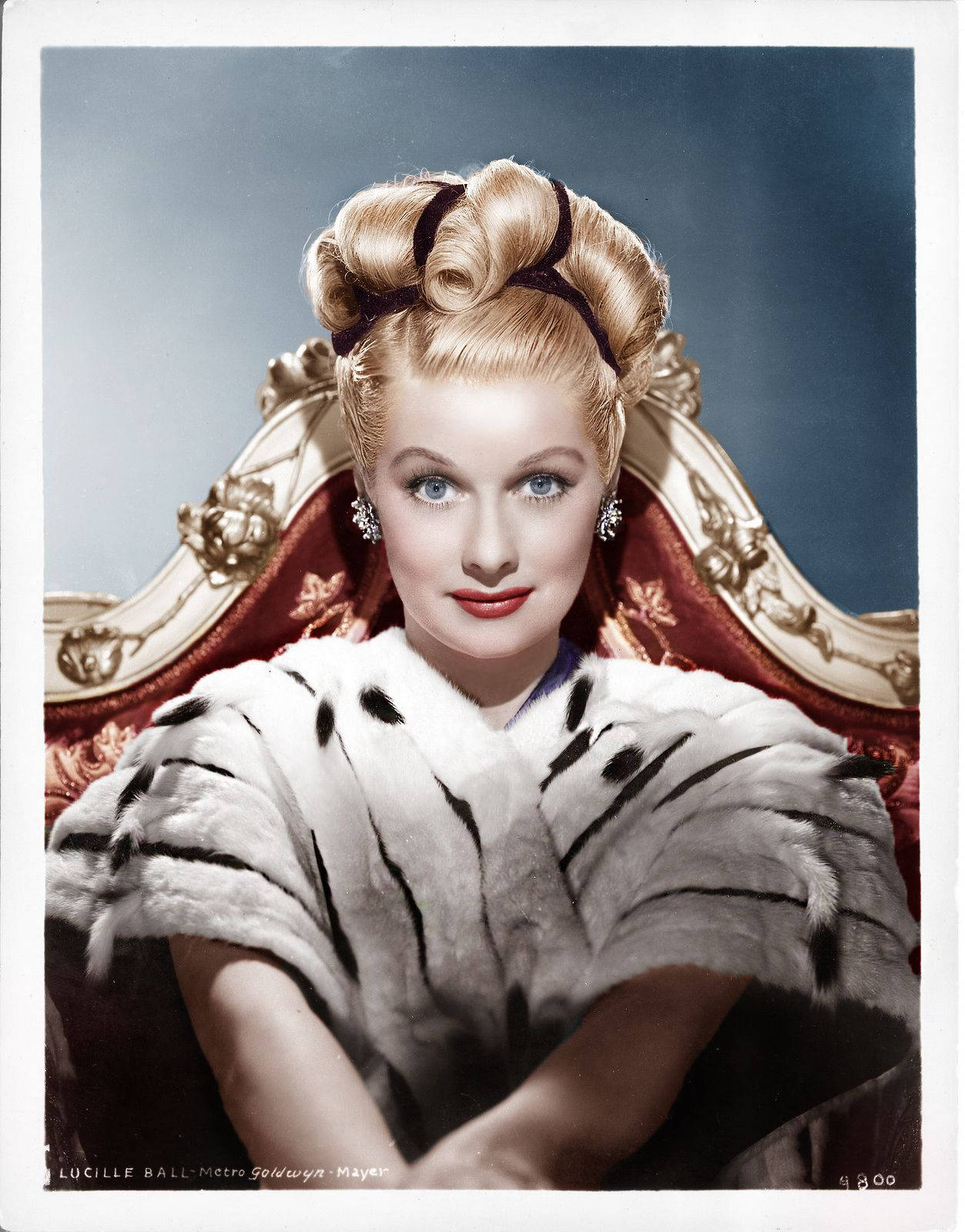 Caption: Lucille Ball Elegantly Sitting On A Red Chair Background