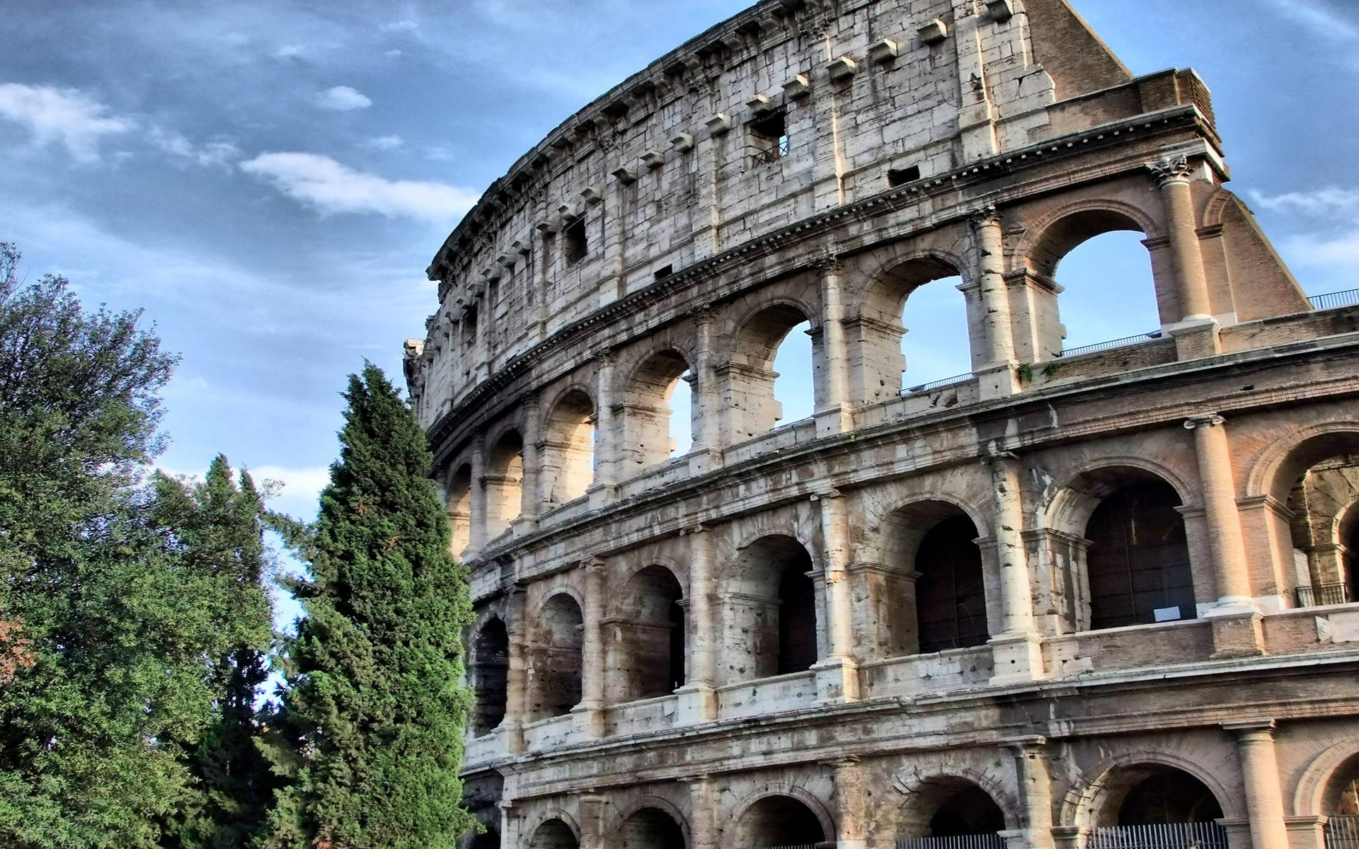 Caption: Majestic Colosseum Underneath A Cloudy Sky Background