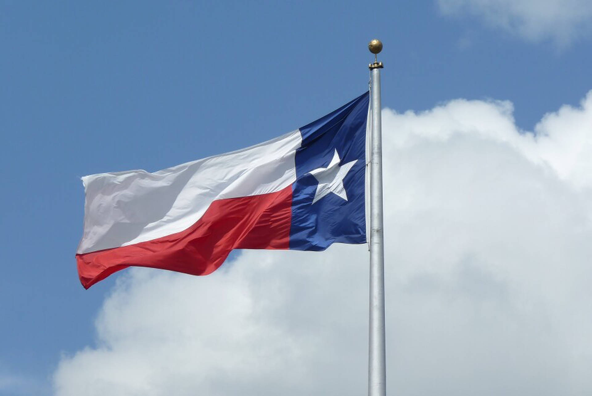 Caption: Majestic Texas Flag Under A Cloudy Sky Background