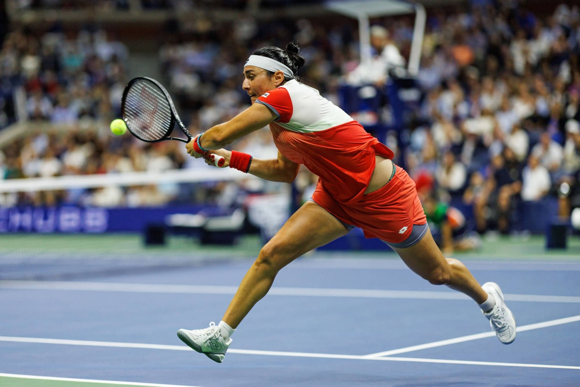 Caption: Ons Jabeur Leaping With Determination In A Competitive Tennis Match. Background