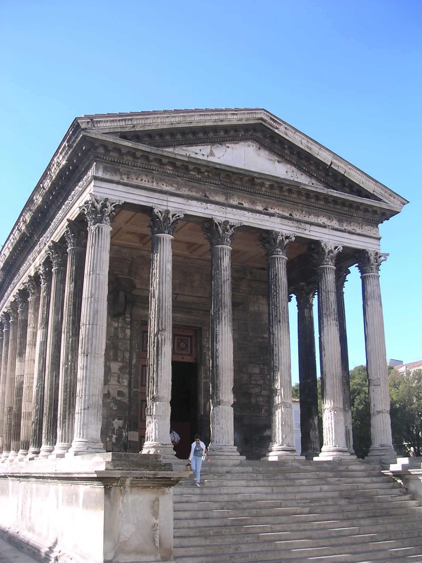 Caption: Person Ascending Steps Of The Historic Maison Carrée Background