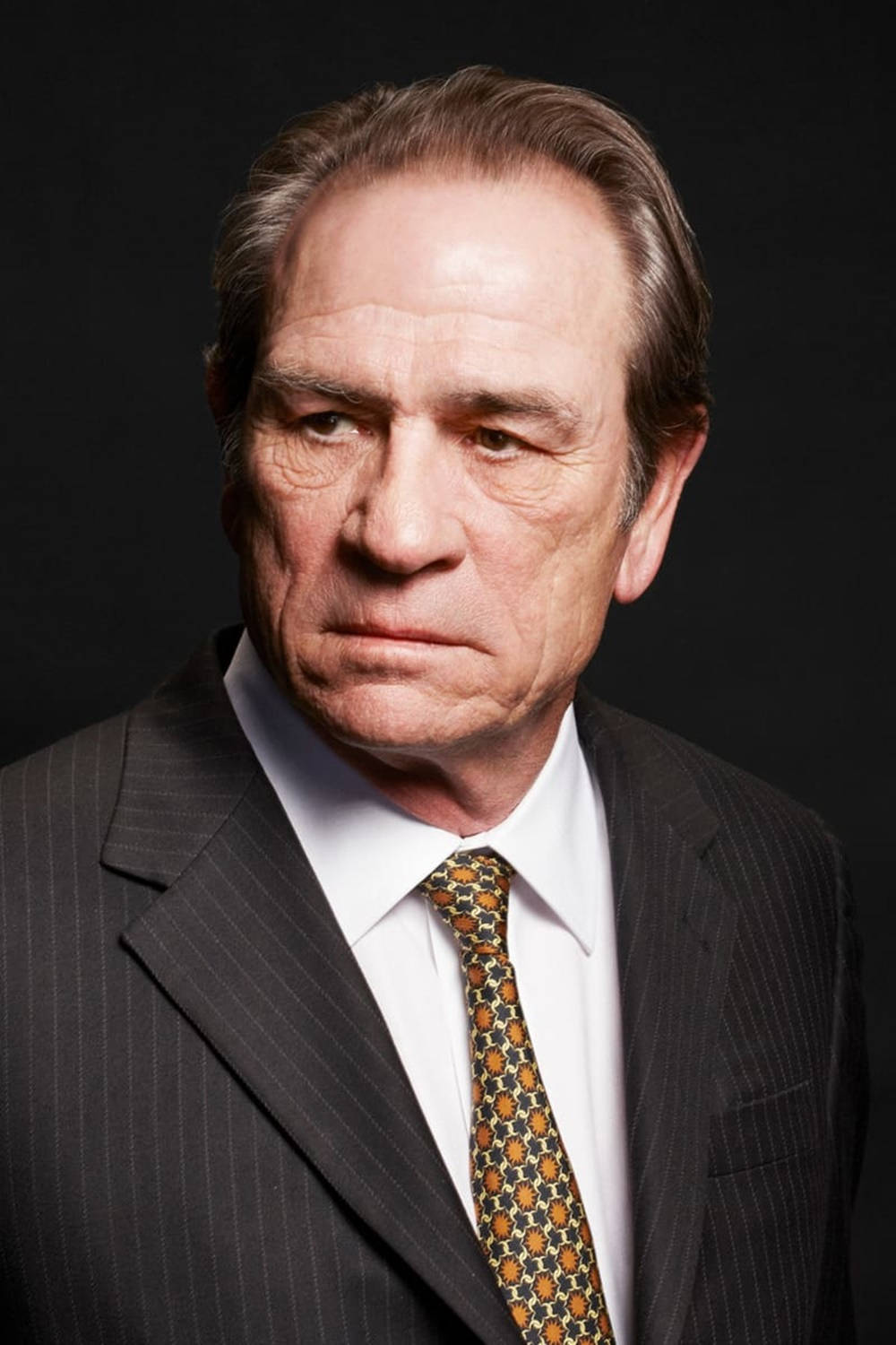 Caption: Portrayal Of Tommy Lee Jones In A Thoughtful Indoor Headshot Background