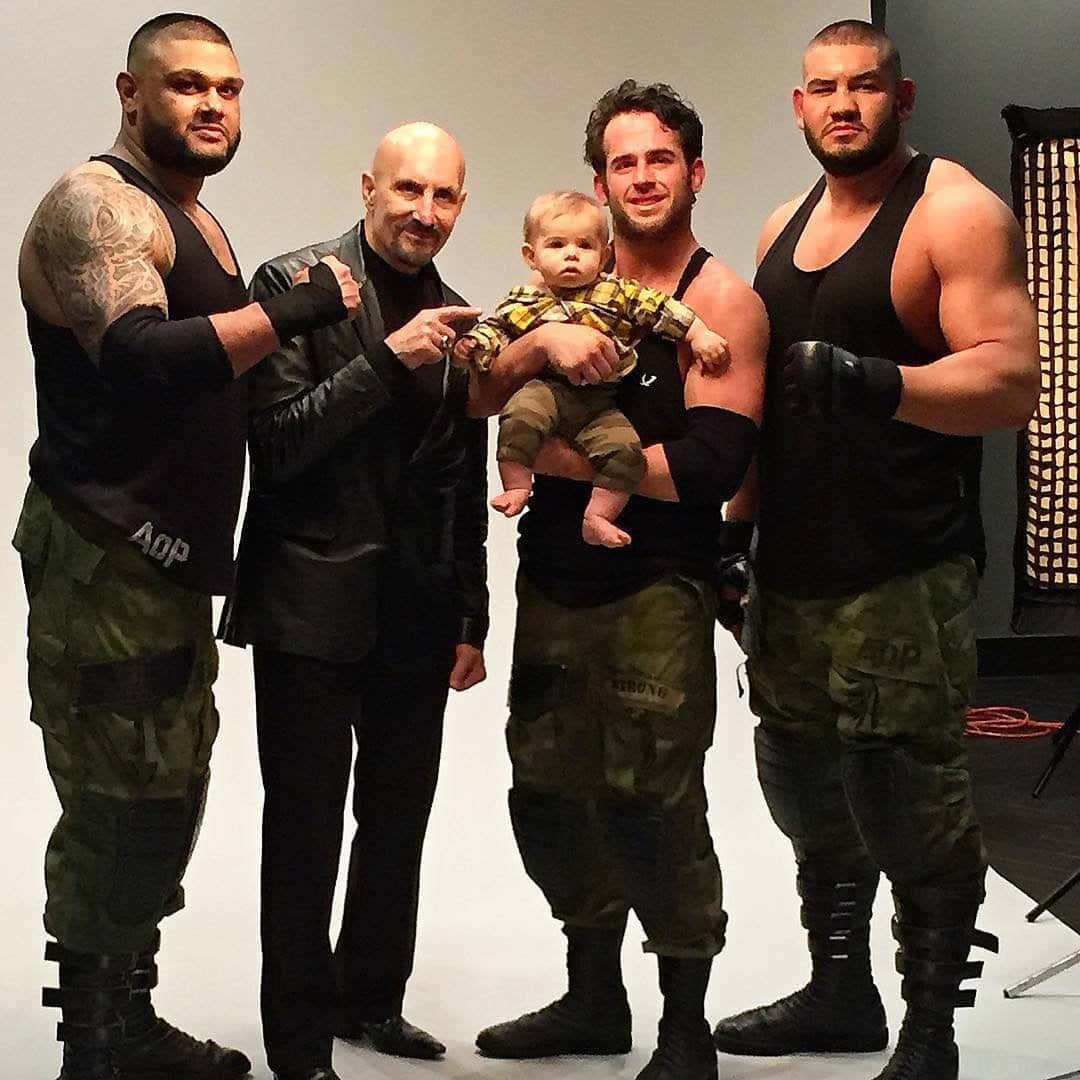 Caption: Roderick Strong With Paul Ellering And Authors Of Pain During A Wrestling Event. Background
