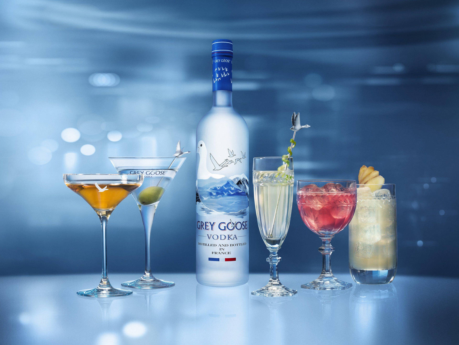 Caption: Sophisticated Enjoyment – Grey Goose Vodka Bottle With Crafted Cocktails Background