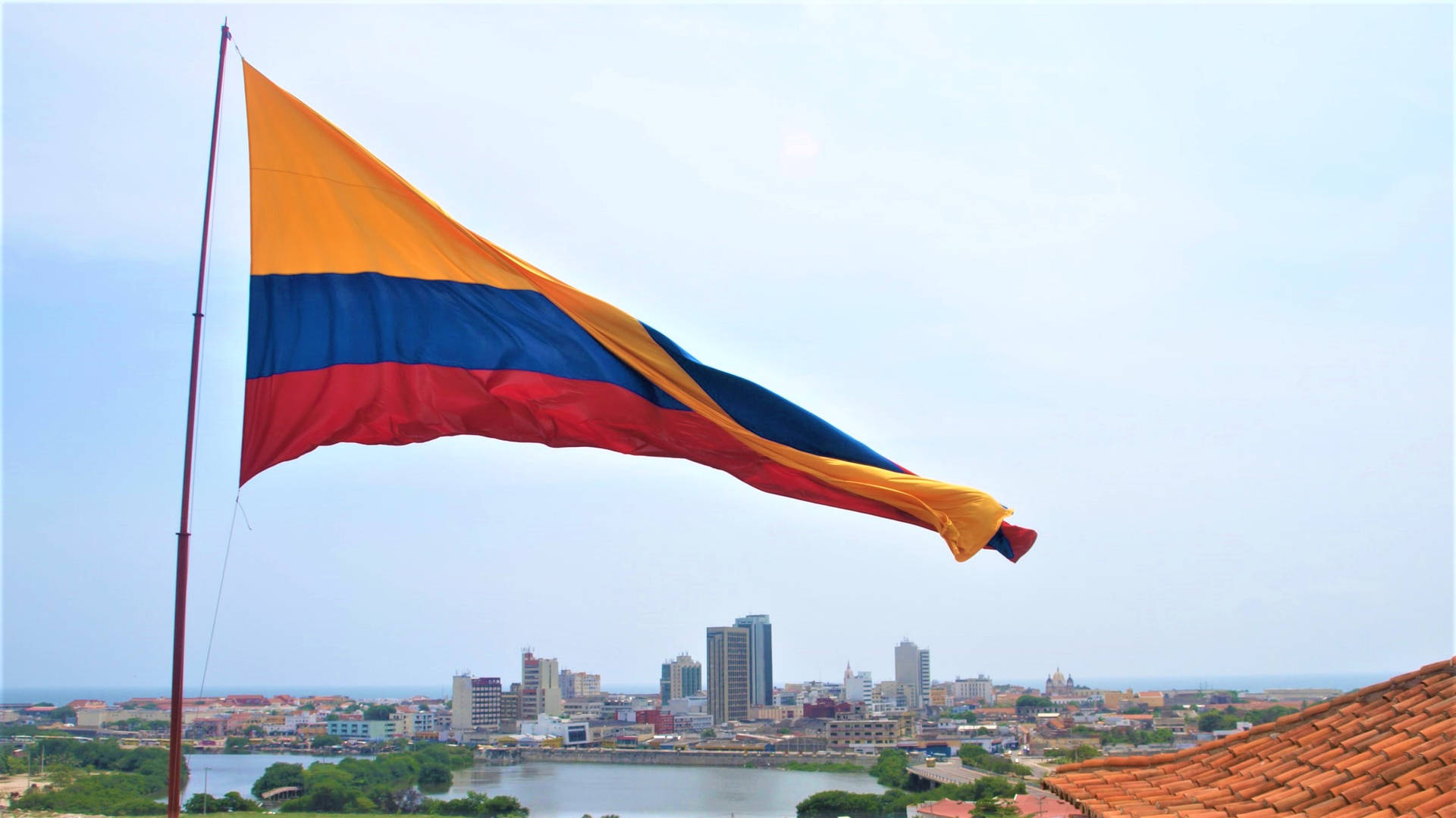 Caption: Vibrant Colombian Flag Waving Proudly Over A Bustling Cityscape. Background