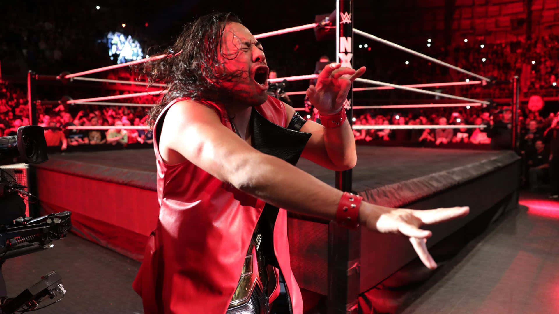 Caption: Wwe Star Shinsuke Nakamura Displaying Rock Horns In Red Vest Background