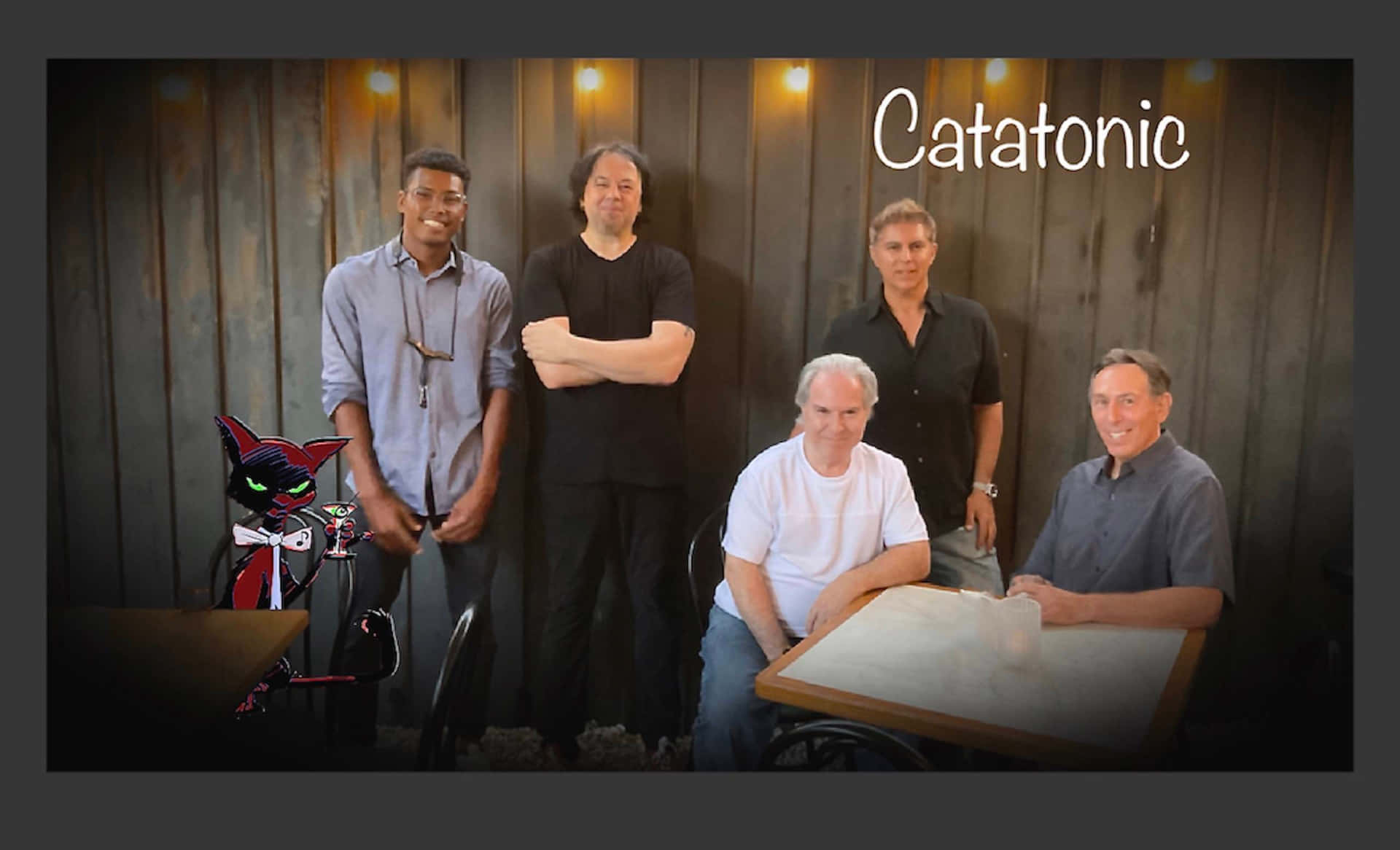 Catatonic - A Group Of Men Standing In Front Of A Table