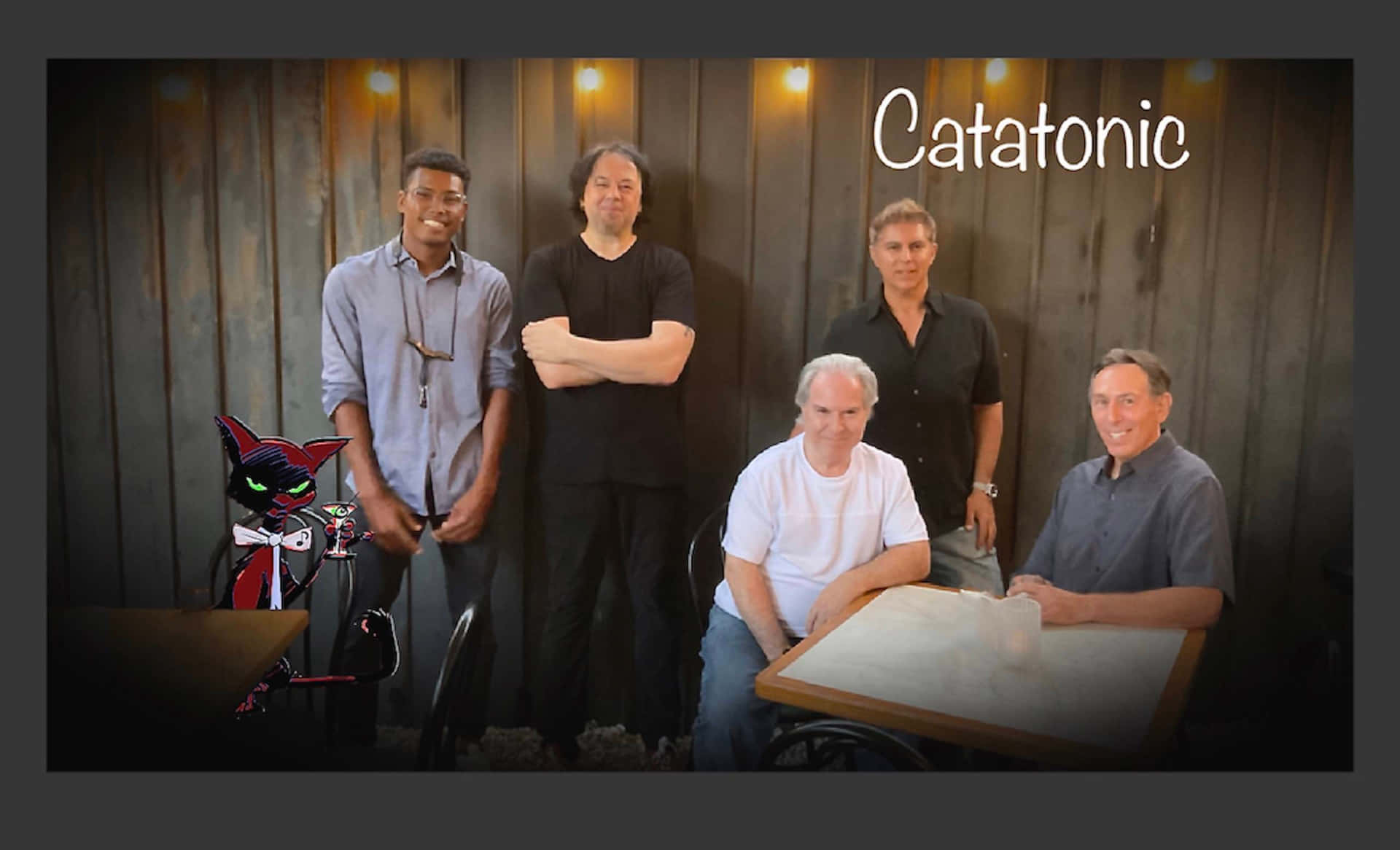 Catatonic - A Group Of Men Standing In Front Of A Table Background