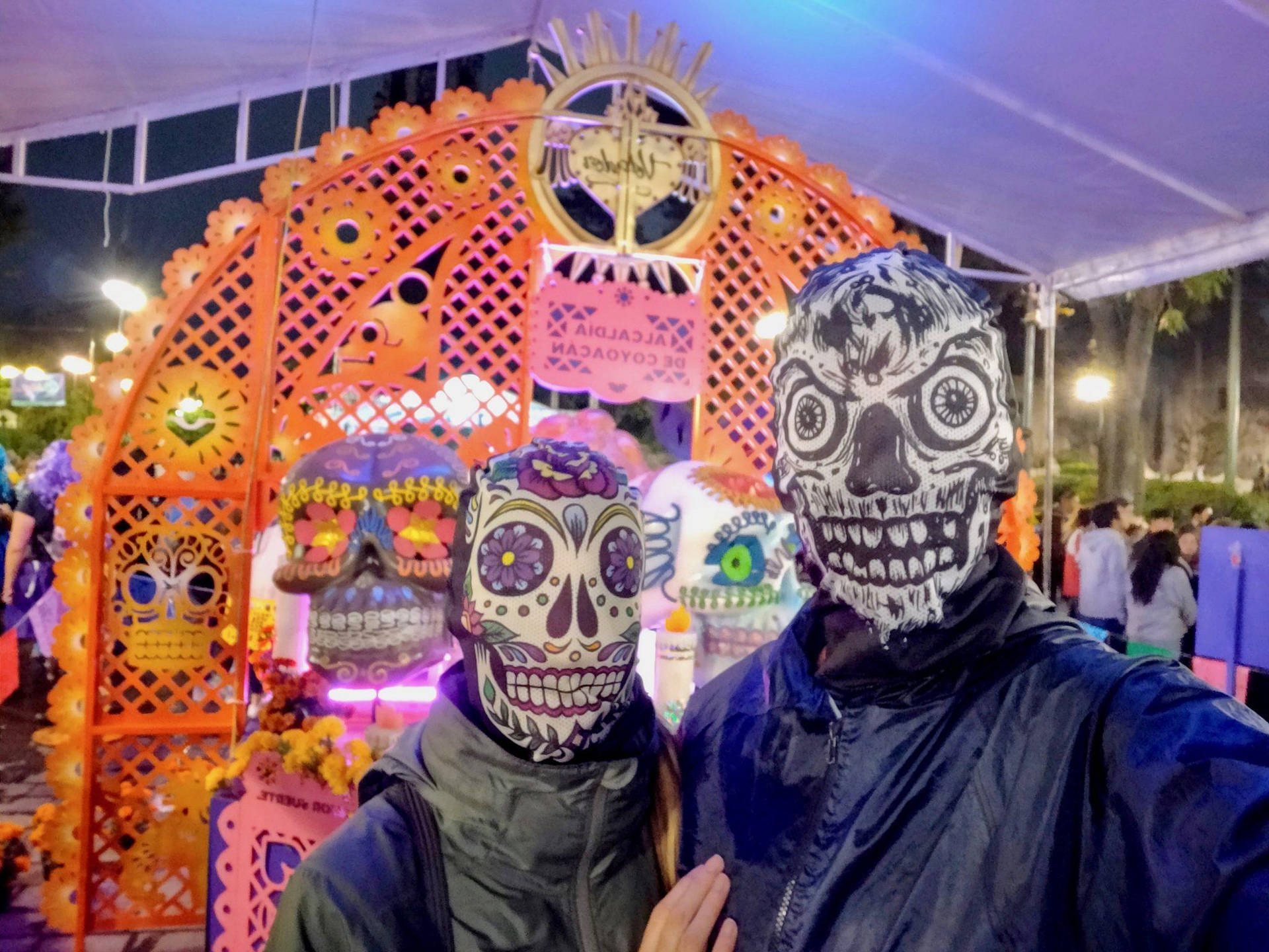 Celebrating Dia De Los Muertos - Two People In Vibrant Skull Masks Background