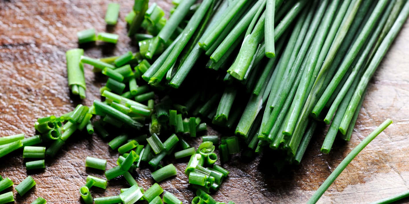 Close-up Of Fresh Green Chives On A Damp Wooden Board Background