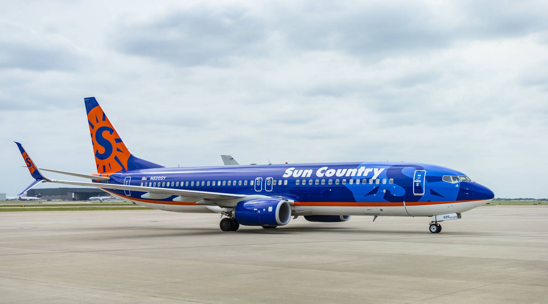 Cloudy Skies Over A Blue Aircraft Of Sun Country Background