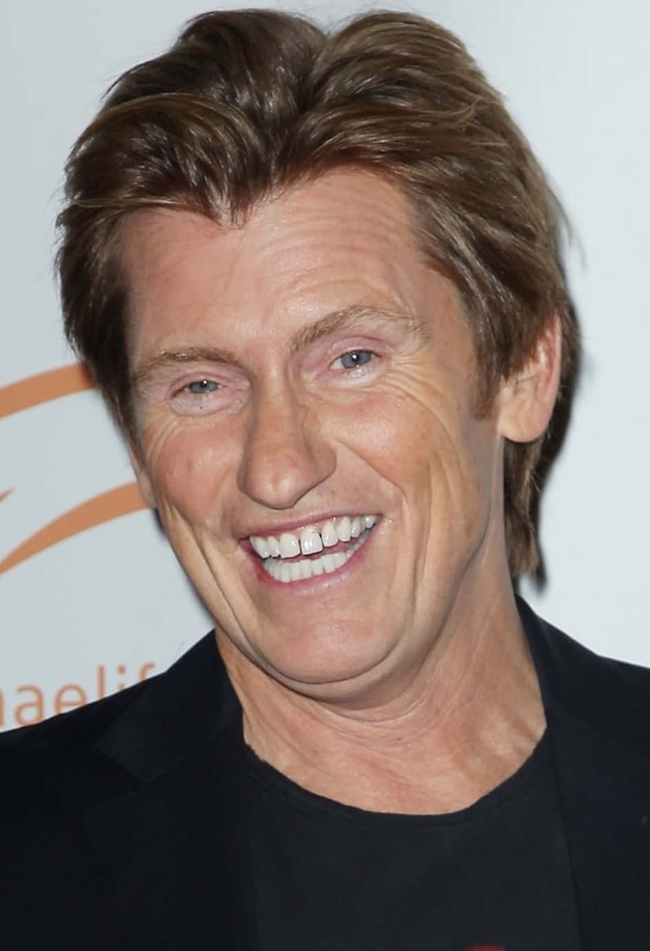 Comedian Denis Leary Leaning On A Brick Wall Background