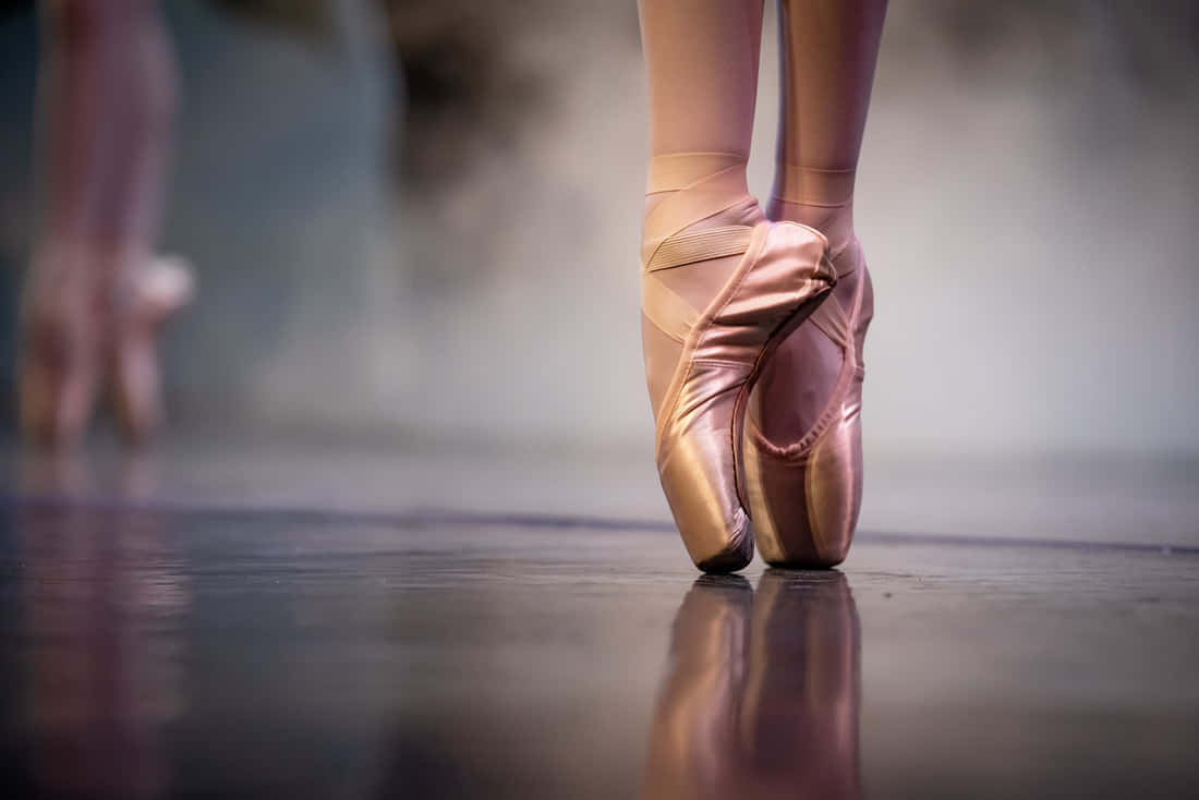 Dancer Effortlessly Gliding Across A Stage In A Pair Of Pointe Shoes. Background