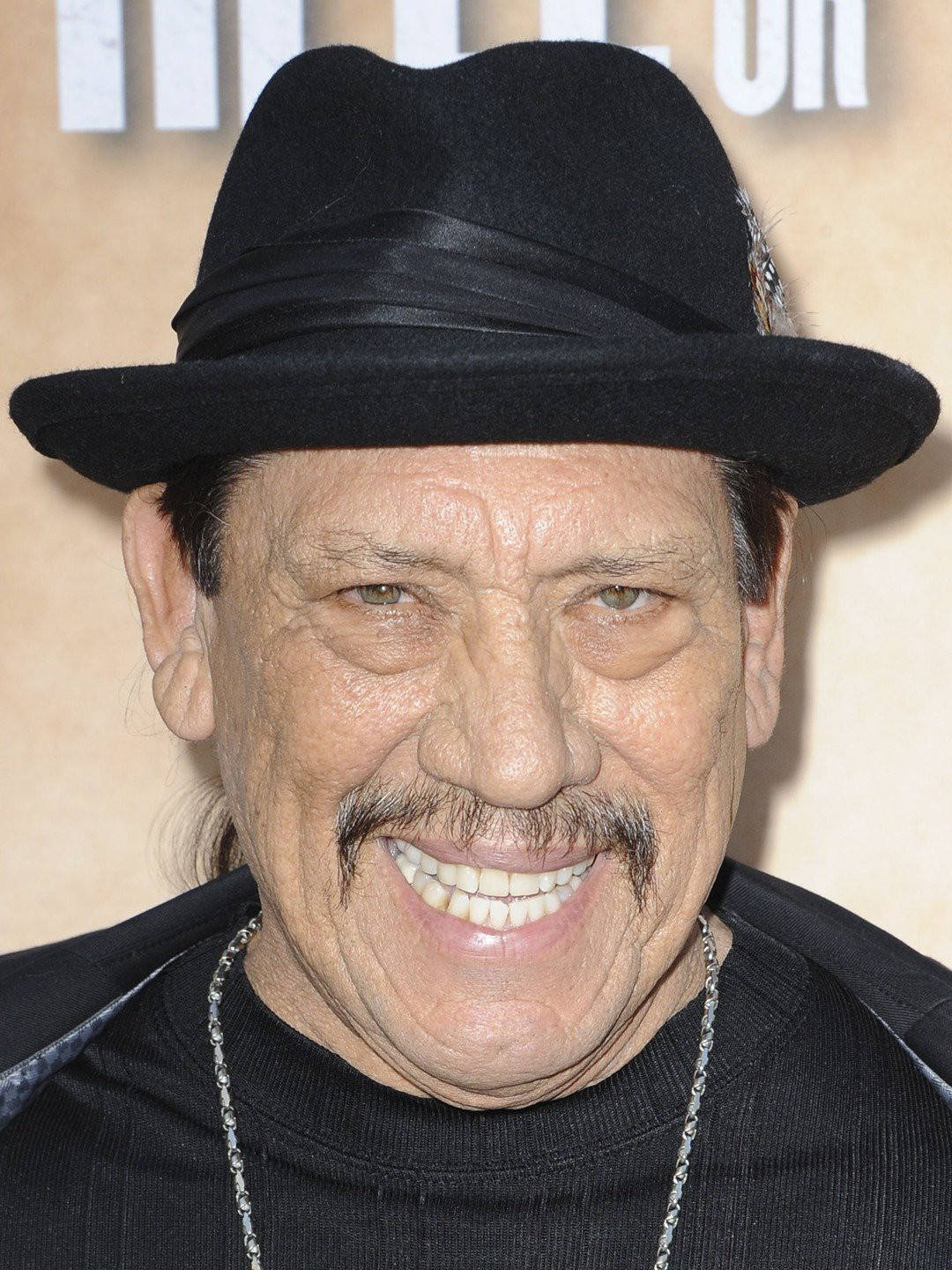 Danny Trejo Smiling In A Headshot Background