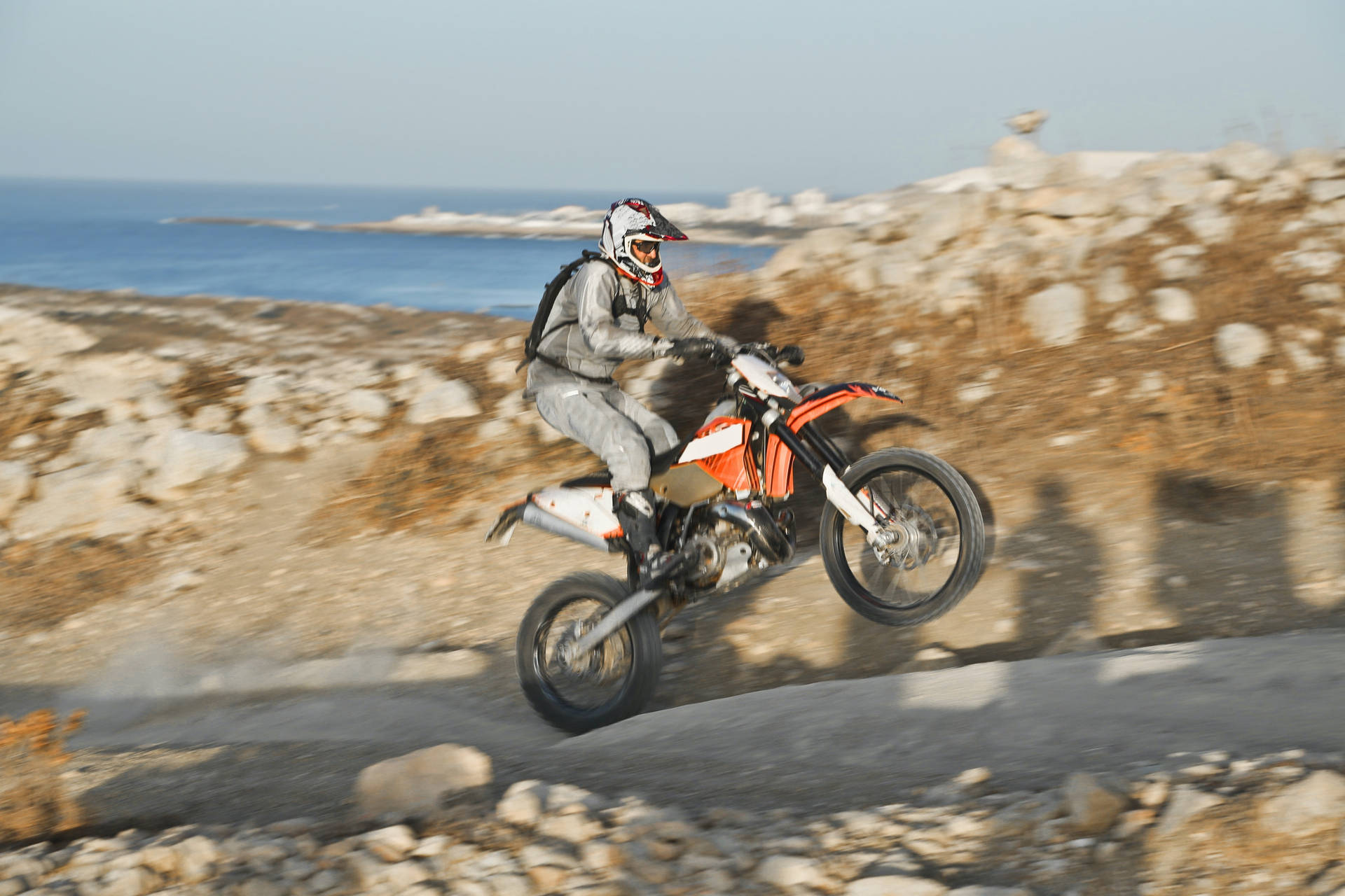 Daredevil Dirtbike Rider Showcasing Wheelie Uphill Background