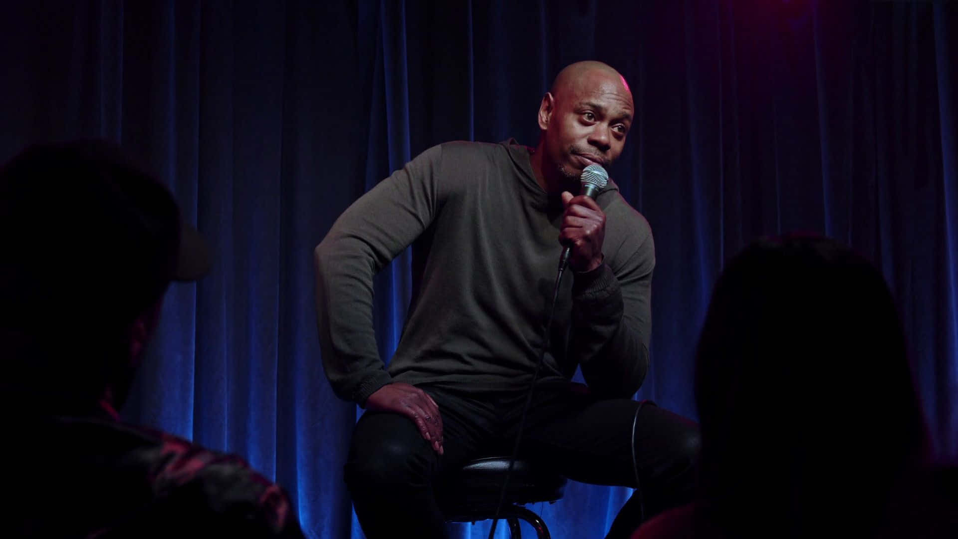 Dave Chappelle On Stage Delivering A Powerful Performance Background