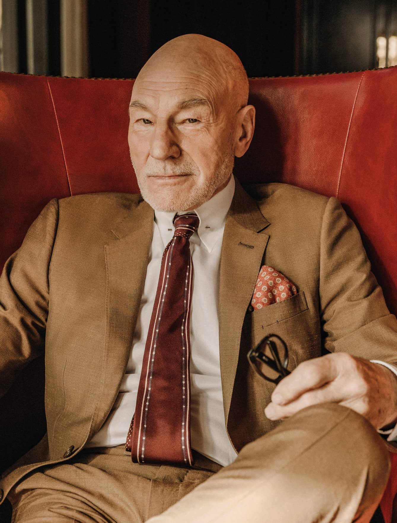 Distinguished Actor Patrick Stewart Relaxing On A Red Couch Background