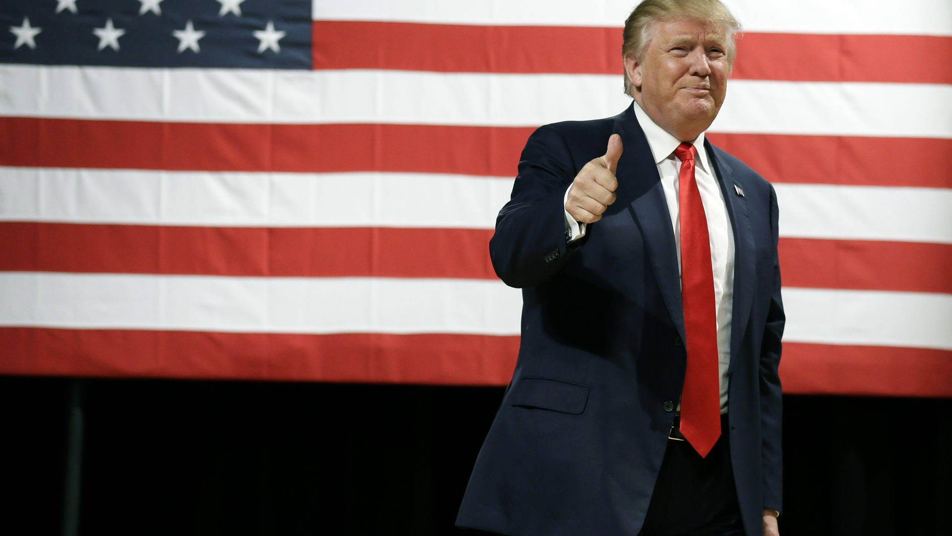 Donald Trump Confidently Raises His Thumb In Approval At The American Flag. Background
