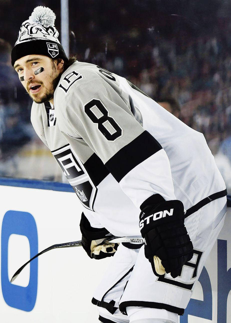 Drew Doughty Leaning Forward While Holding Hockey Stick In Front Background