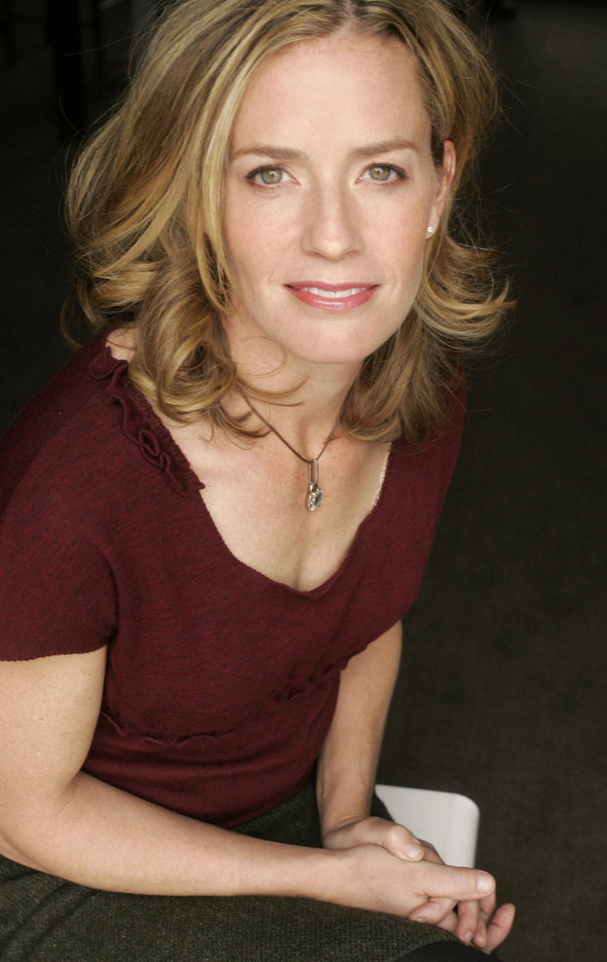 Elisabeth Shue Wearing Maroon Top With Both Hands On Lap Smiling Background