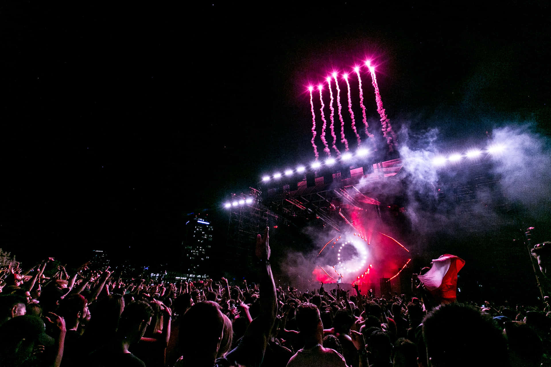 Energized Music Festival Crowd Under A Vibrant Sunset Skyline Background