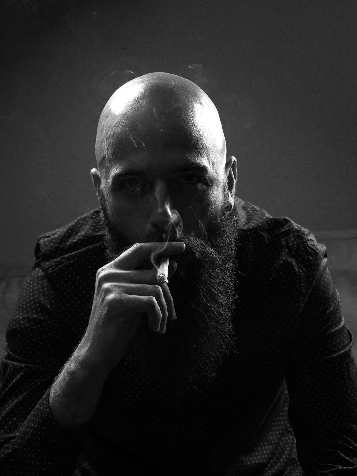 Enigmatic Bald Man Relishing The Pleasure Of Smoking Background