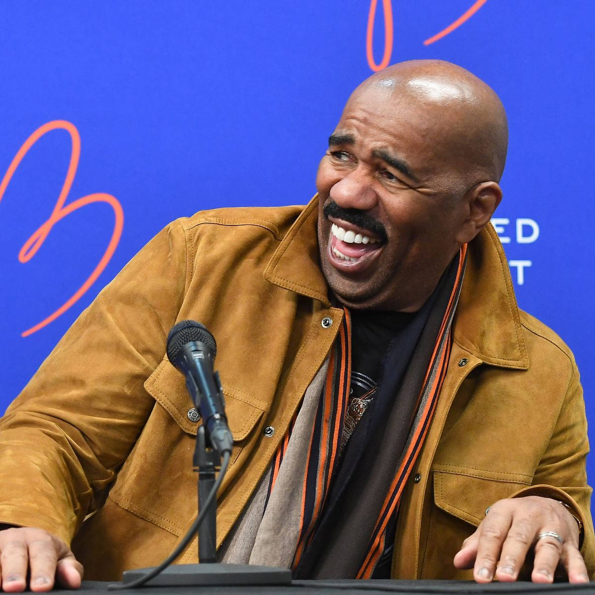 Enthusiastic Steve Harvey Holding A Microphone And Laughing Background
