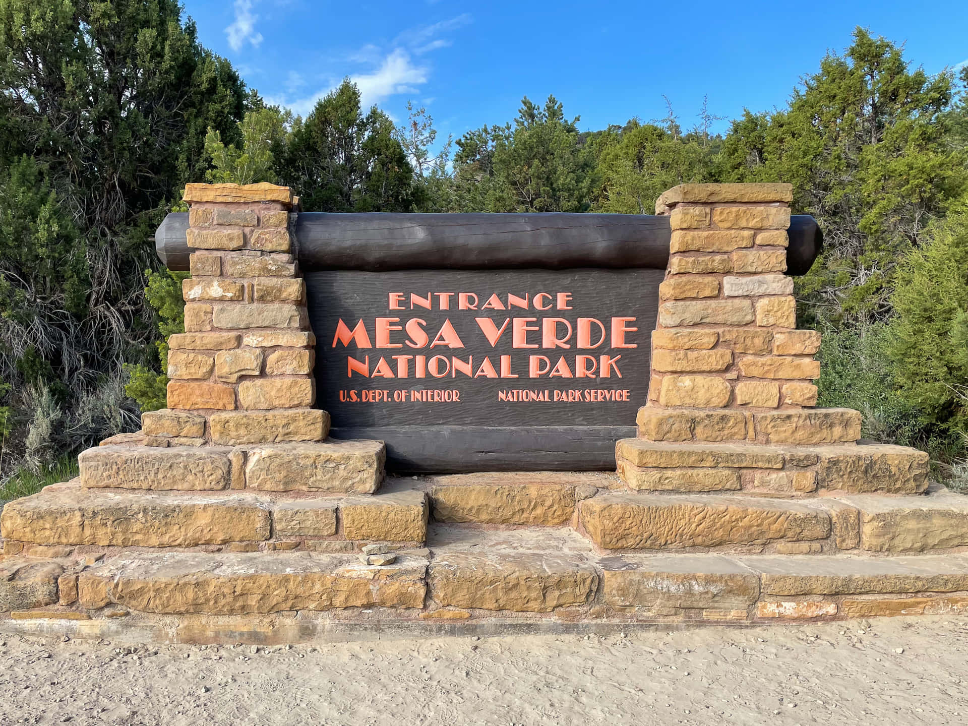 Entrance Sign Of Mesa Verde National Park Nestled Amidst Lush Greenery Background