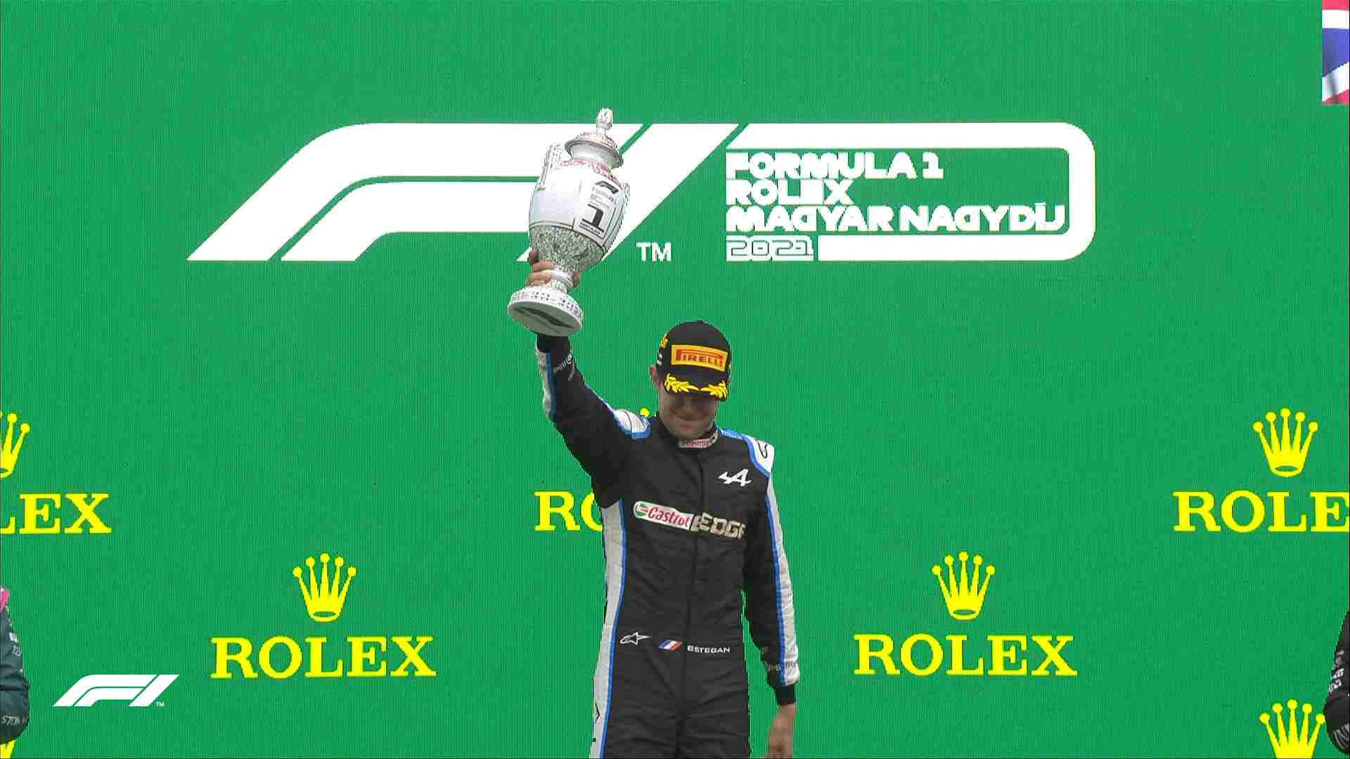 Esteban Ocon Raising Trophy In Victory Background