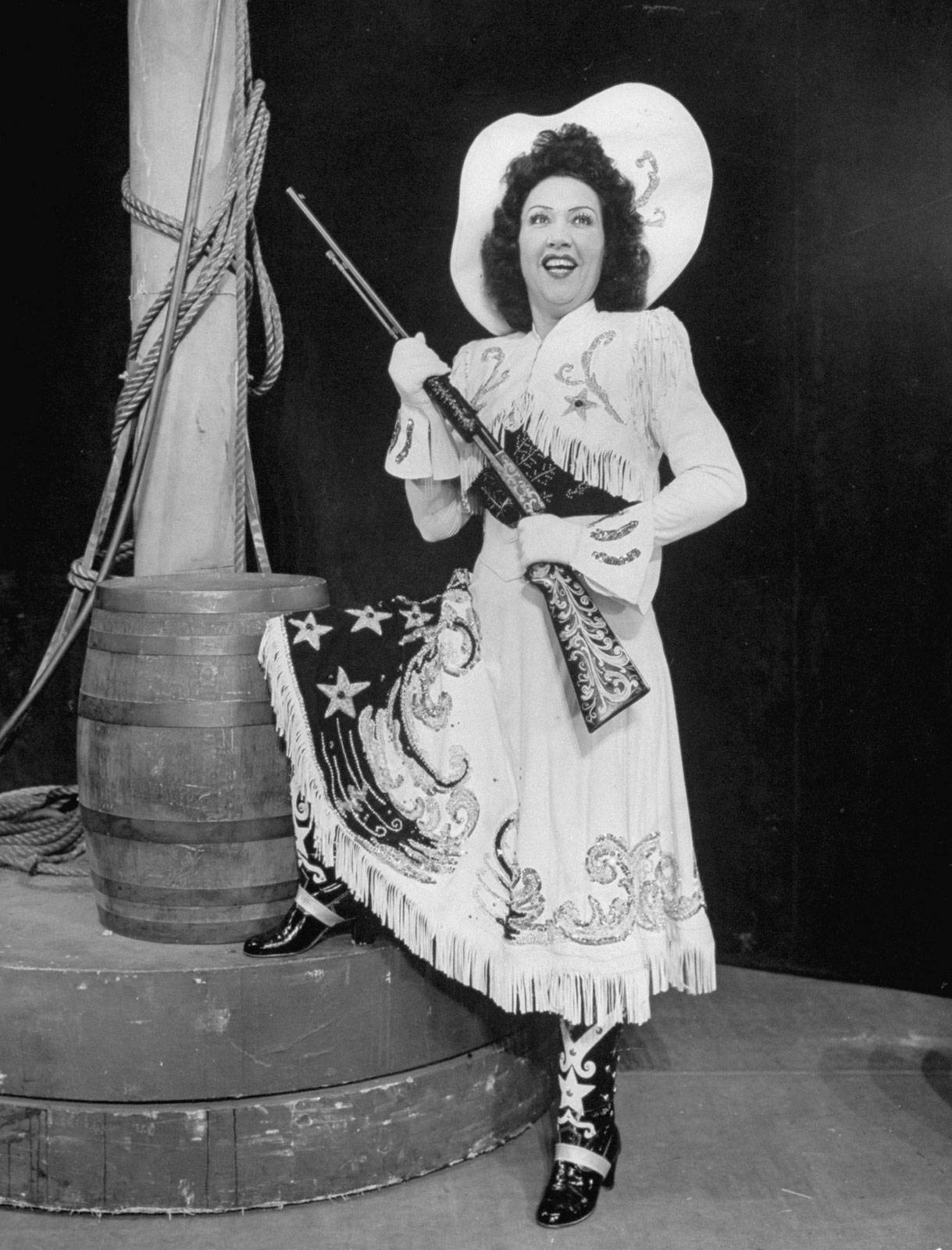 Ethel Merman Holding A Rifle By A Barrel Background