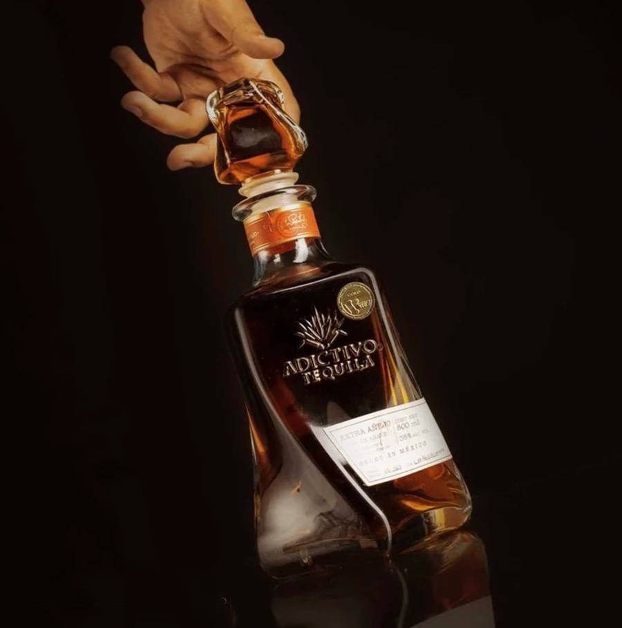 Exquisite Bottle Of Dark Amber Adictivo Tequila Reposado Background