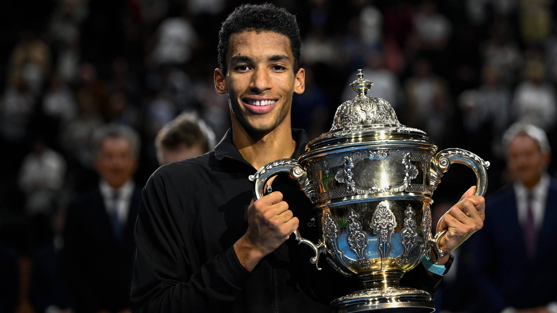 Felix Auger-aliassime Triumphantly Lifting A Trophy Background