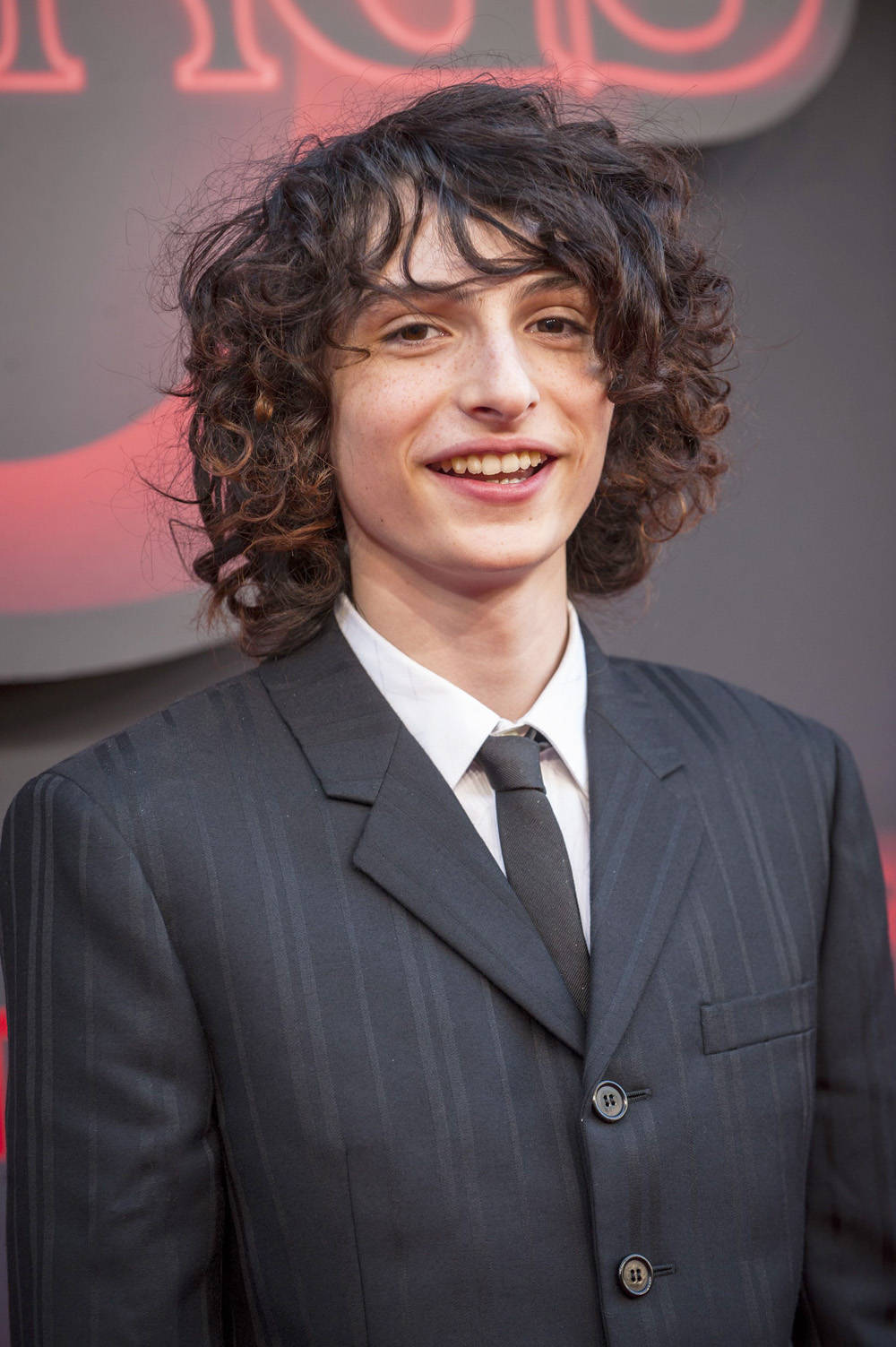 Finn Wolfhard Smiling On Stage Background