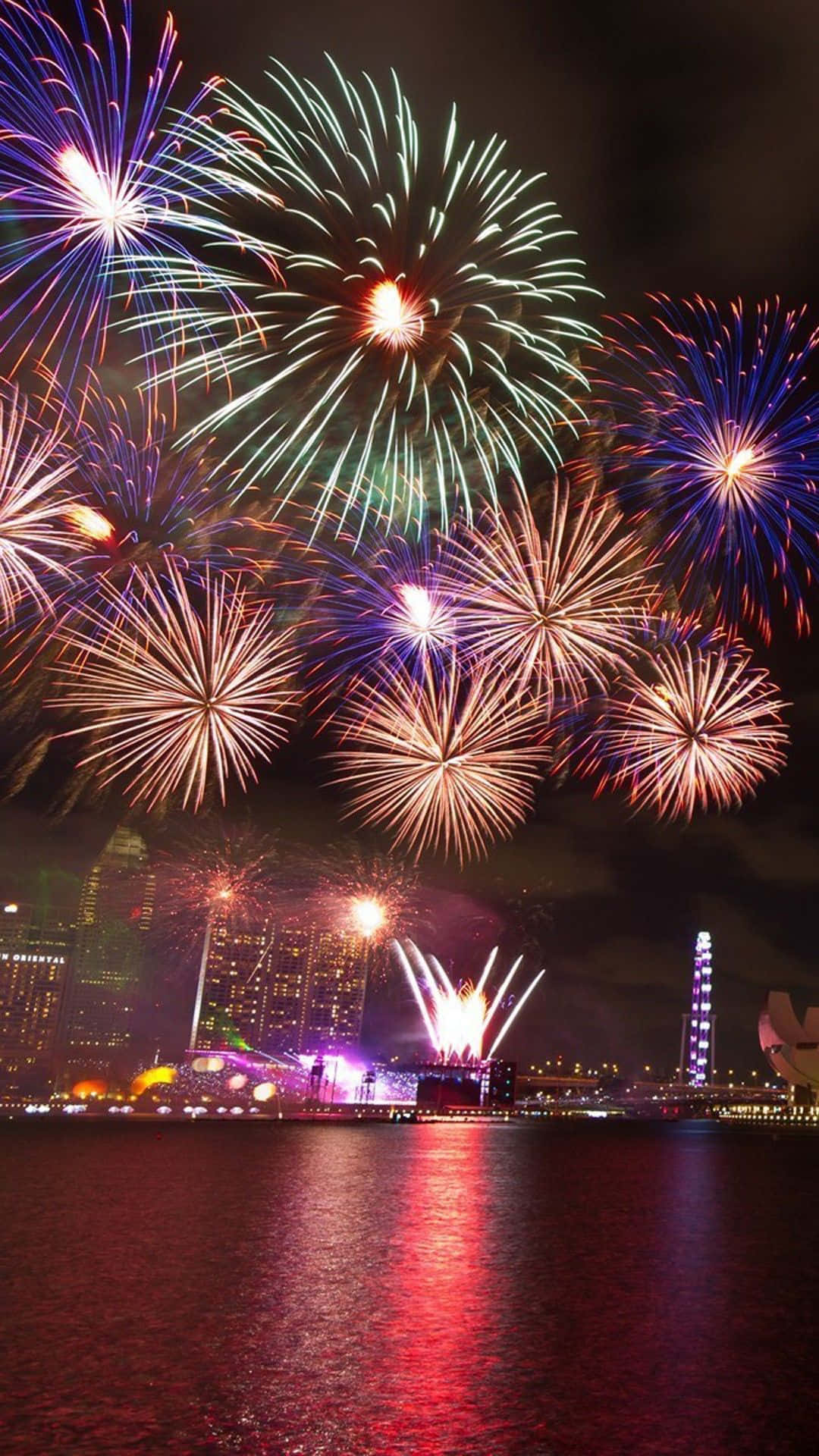 Fireworks Over The Water With A City In The Background Background