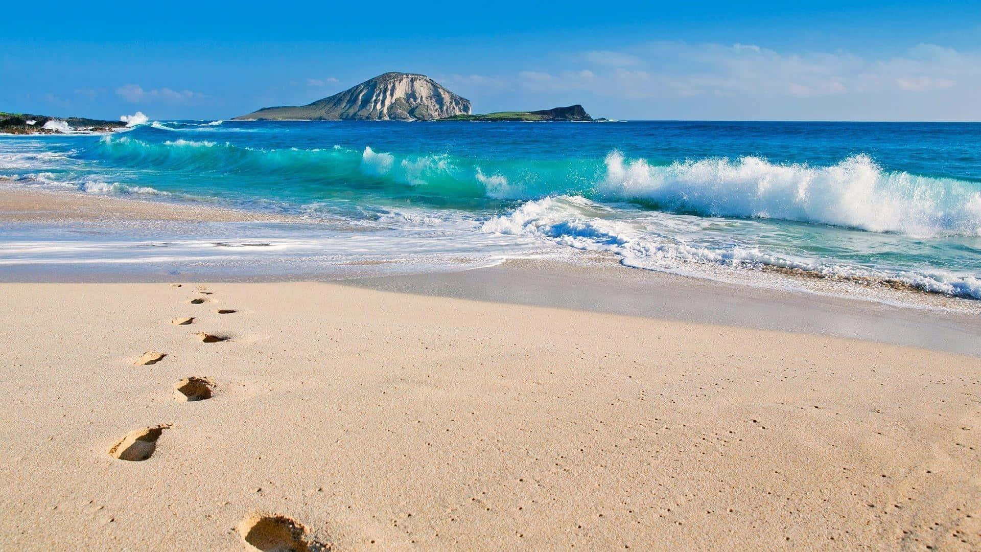 Footprints On A Beach With Waves And An Island Background