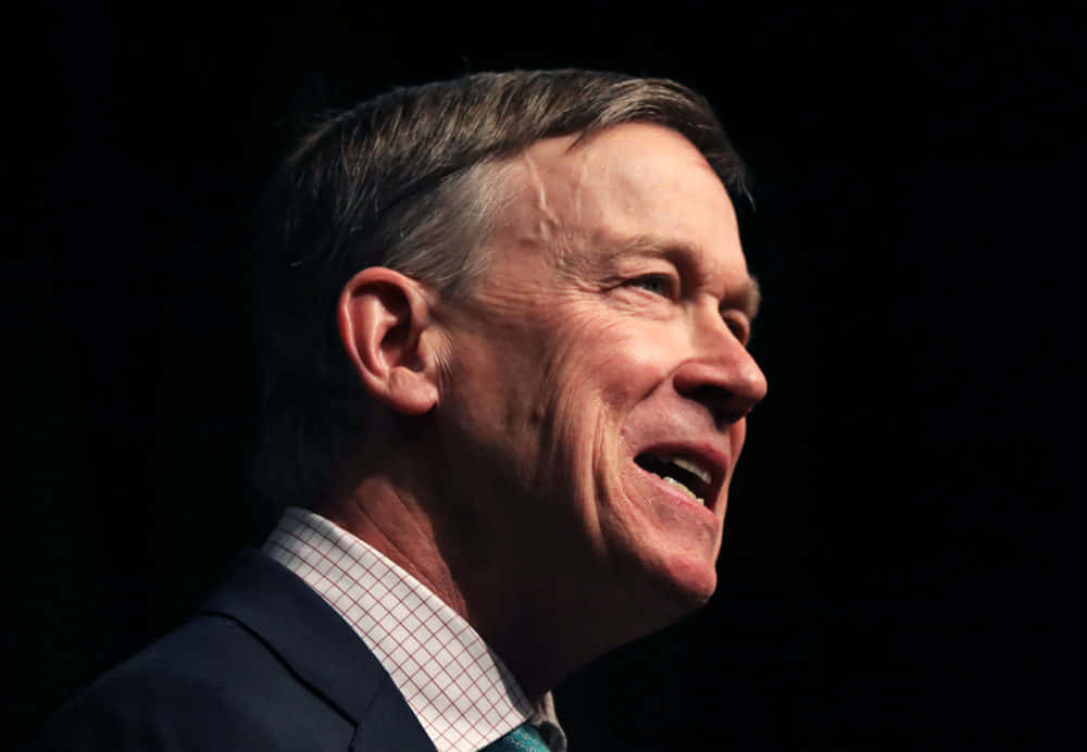 Former Governor, John Hickenlooper, Delivering A Speech Against A Black Backdrop. Background